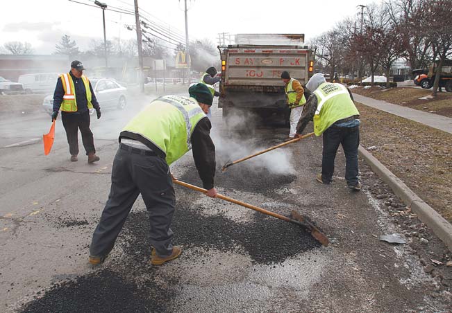 Frank Kordupel , with flag, of the Mahoning County Engineer’s Office, supervises a group of minimum-security and day-reporting inmates from the county jail who fill potholes on South Avenue near Midlothian Boulevard. They were at work Monday. The county used four inmates from the day-reporting program to help fill potholes, which are in abundance because of the wave of freezing and thawing to hit the area.