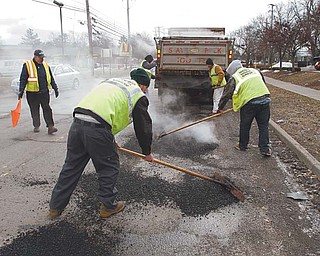 Frank Kordupel , with flag, of the Mahoning County Engineer’s Office, supervises a group of minimum-security and day-reporting inmates from the county jail who fill potholes on South Avenue near Midlothian Boulevard. They were at work Monday. The county used four inmates from the day-reporting program to help fill potholes, which are in abundance because of the wave of freezing and thawing to hit the area.