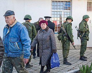 A woman walks outside the General Staff Headquarters of the Ukrainian navy as unidentified gunmen stand guard in Sevastopol, Ukraine, on Monday.

