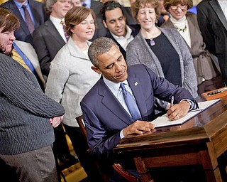 President Barack Obama, surrounded by supporters of the president’s memorandum, signs a Presidential Memorandum directing Labor Secretary Tom Perez to modernize overtime protections. Obama signed the memorandum Thursday in the East Room of the White House in Washington.