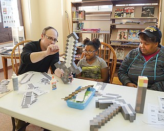 John Waller, assistant supervisor of reader services at the main branch of the Public Library of Youngstown and Mahoning County, works on a Minecraft Is Your Craft project with Heaven Harris, 7, and her mother, Tracie Gilmore, 39, both of Youngstown. The program is based on a popular video game called Minecraft.