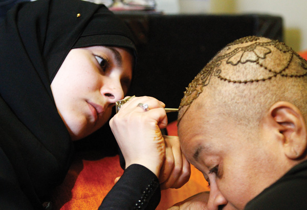 Lamia Alfares, a local Henna artist, draws a Henna crown on the head of Monaca Beasley-Martin at the Calvin
Center in Youngstown. Beasley-Martin has alopecia, a condition in which a person is allergic to his or her own hair and becomes bald.