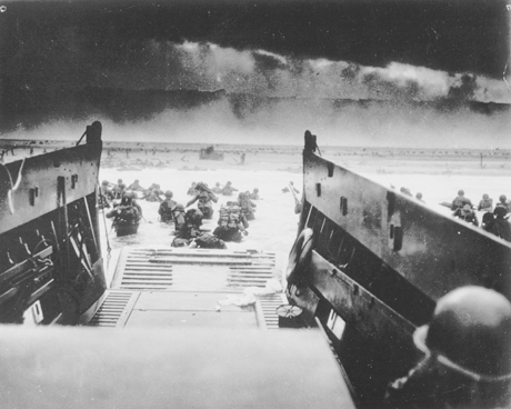 In this image provided by the U.S. Coast Guard, while under attack of heavy machine gun fire from the German coastal defense forces, these American soldiers wade ashore off the ramp of a U.S. Coast Guard landing craft, during the Allied landing operations at Normandy, France on June 6, 1944. (AP Photo/U.S. Coast Guard)