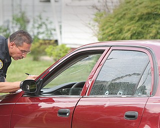 Pete Bonilla, a Youngstown police officer, inspects bullet damage to a car belonging to a man who was shot in the arm at Jackson Street and Himrod Avenue on Monday afternoon.