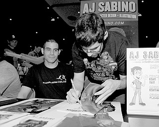 Local artist AJ Sabino of Cortland signs a piece of original artwork during the 2014 All-AmeriCon comic book convention. Rocco Sabino of Cortland also is pictured.
