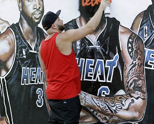 A man, who did not wish to be identified, spray paints "Thanks LeBron," over a vandalized mural of the Miami Heat players featuring LeBron James, Friday, July 11, 2014, in Miami. James is returning home to Ohio, reversing the decision he made four years ago that led to two NBA titles in Miami and crushed Cleveland Cavalier fans. "I just don't want people disrespecting LeBron," the man said, " He did so much for the city. I've been waiting all day to get off work to do that." (AP Photo/Wilfredo Lee)