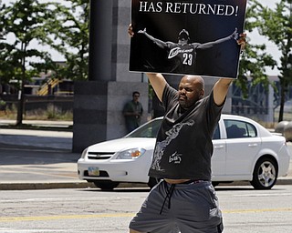 Graphic designer Alvin Smith holds up a poster in the street outside Quicken Loans Arena in Cleveland Friday, July 11, 2014, heralding the return of NBA basketball star LeBron James. James, who left the Cavaliers four years ago to join the Miami Heat, announced earlier he would return to the Cavaliers. (AP Photo/Mark Duncan)