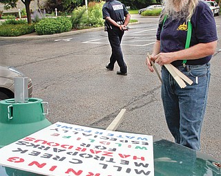 Jack Malley, above, of Youngstown examines his sign saying: “Warning: Mill Creek MetroParks: Hazardous for wildlife, especially waterfowl.” The park police officer in the background told him he wasn’t allowed to display the sign on his car in a park parking lot Monday, outside a park board meeting. 