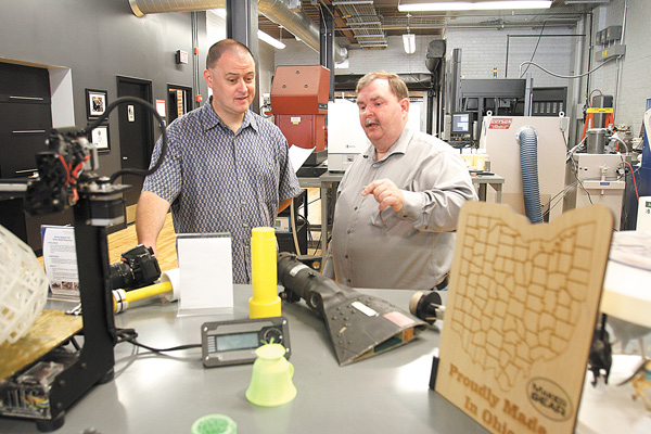 T.J. McCue, a national author, left, watches as Kevin Collier of America Makes shows how a part made through
3-D manufacturing helps fix the bearing for an Apache helicopter.