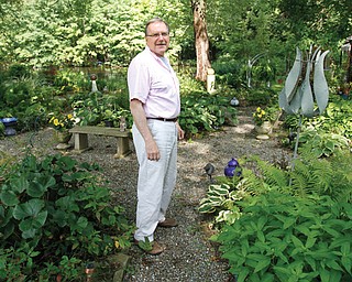 The Rev. David W. Merzweiler, left, better known as Pastor Dave, stands on a gravel path in the expansive garden he has worked on behind the rectory at St. Catherine Church, 1254 Grandview Road, Lake Milton, where he lives.
The green oasis of plants also features garden art, statues, four fountains, a pond, wind chimes and an enclosure
with four peacocks.