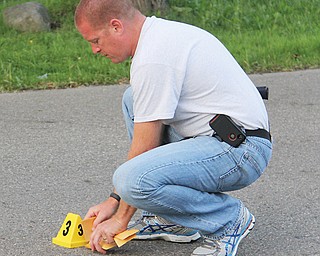 A member of the Youngstown Police Department collects a gun shell casing as evidence from the middle of Winona Drive on Youngstown’s South Side after a shooting there Sunday evening. At least one person died in the
gunfire.