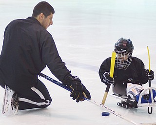 Coach Adam Chudnofsky of Boardman kneels next to Joshua Kurth II, 4, of Canfield and encourages him during a sled hockey practice at The Ice Zone in Boardman.