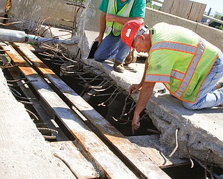 Randy Partika, Mahoning County bridge engineer, left, and Tony Gaglione of B.G. Trucking & Construction of North Lima examine the underlying steel where an expansion joint is being replaced on the Market Street Bridge in Youngstown on Monday. Traffic will remain reduced to one lane in each direction on the bridge through
November. 