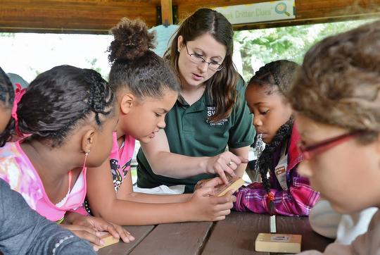 Jeff Lange | The Vindicator  Amy Reeher of the Trumbull Soil & Water Conservation District helps (from left; Shi'nece Honzy 9, Trinity Brown 9, and second from right Aniya Starks 9 of McGuffey) determine which creatures are present in their water pollution activity, Tuesday morning at Perkins Park.