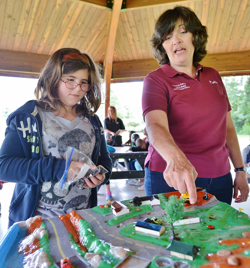 Jeff Lange | The Vindicator  Education Coordinator of the Trumbull Soil & Water Conservation District Kelly Hardval instructs Ashleigh Ellison 9 of McGuffey where to place 'manure' (chocolate chips) on the water table during Tuesday's demonstration at Perkins Park.