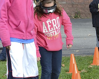 Katie Rickman | The Vindicator.Thomas Barnes, 13, on left who is a PANDA Leadership Club student volunteer assists Leah Barone, 11, around the cones while she wears goggles that simulate the affects of driving under the influence of alcohol during the tailgate party at Struthers Middle School on Wednesday, Oct. 29, 2014.