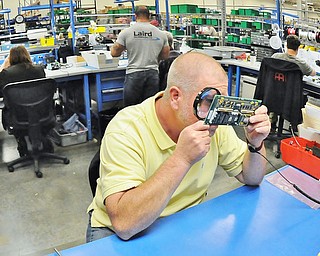 Jeff Lange | The Vindicator  Quality Technician for Laird Tom Clarke carefully examines an encoder board under a magnifying glass. Tom is checking to make sure all of the pins are properly soldered to the encoder board, Thursday afternoon during a tour of Laird.