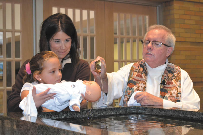 SPECIAL TO THE VINDICATOR
Every year first-graders at Holy Family School get to experience a hands-on lesson about the sacrament of baptism. They take baby dolls from home and teachers assign the roles of parents and godparents to students. The Monsignor William Connell blesses the “parents” and “godparents” and baptizes the dolls. Above are first-grader Julianna Ramos with teacher Kristin McCloud and Monsignor Connell, pastor of Holy Family Parish, “baptizing” baby doll Jason Max.