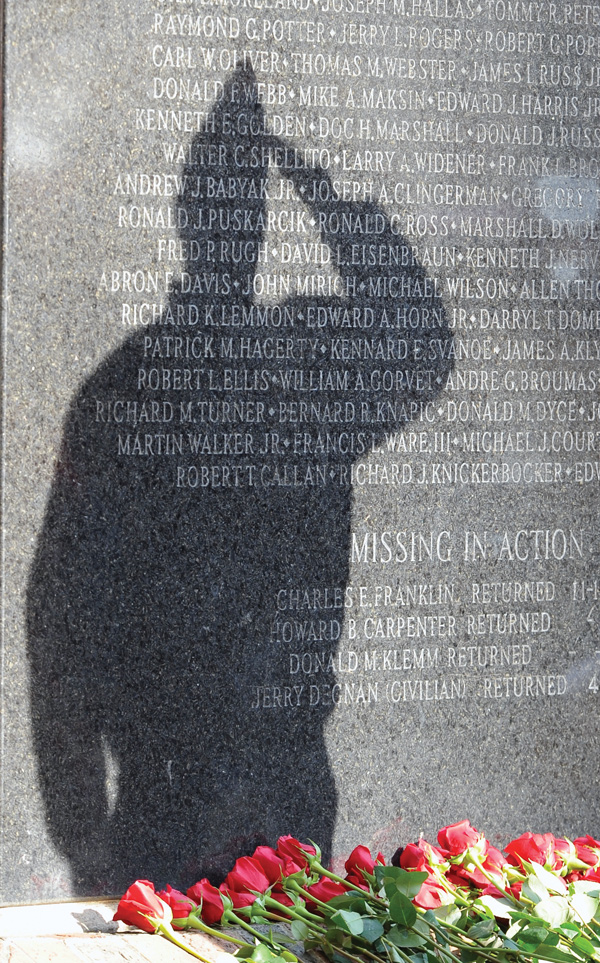 A veteran pays respects during the Reading of the Names portion of the ceremony at the Mahoning County Vietnam War memorial downtown. Roses placed at the monument honor the fallen soldiers.