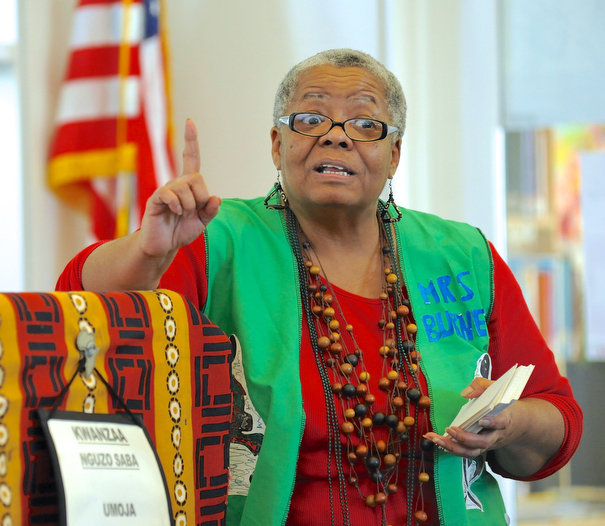 Jeff Lange | The Vindicator  Gladys Burnett of Friends of Youngstown & Mahoning County Public Library stands beside the podium as she explains that Kujichagulia means self determination, Saturday afternoon during the second day of Kwanzaa celebration at the East Branch of the Public Library of Youngstown and Mahoning County.