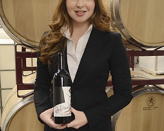 Katie Rickman | The Vindicator.Marisa Sergi, 21 of Youngstown stands near wine barrels and holds a bottle of her wine at Luva Bella Winery in Lowellville on Tuesday, Dec. 30, 2014. Sergi is a senior at Cornell University and as a part of a final project developed a start-up called RedHead Wine.