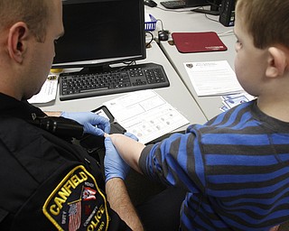        ROBERT K. YOSAY  | THE VINDICATOR..school resource officer Steve Garstka  works on Carson Nagy 's  form.. of placing his fingerprints on the form.. over 900 students hope to be done..part of a PTA/School/ and Canfield PD initiative... students in k-4 in the Canfield Schools will have an Identity Kit done in school with their fingerprints and then sent home to the parents.