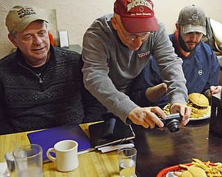 Katie Rickman | The Vindicator.Anthony Fuda leans over the shoulders of JT Tranovich on left James Chismark and takes a picture of a burger and during the Burger Guyz visit to the Courthouse Grill in Warren on Wednesday, Jan. 28, 2015.