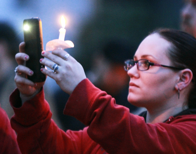 A woman takes a photo during a vigil for 3 people killed in a Youngstown house fire.