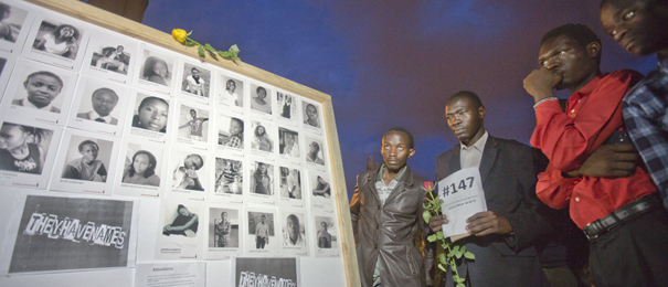 Kenyans look at a board showing some of the faces and names of the victims of the Garissa attack, during a vigil at Uhuru Park in Nairobi, Kenya Tuesday, April 7, 2015. Students and other Kenyans gathered at dusk to honor and remember the victims, lighting candles, holding flowers, reading their names aloud, and erecting a white wooden cross for each of those who were killed in the Garissa University College attack. (AP Photo/Ben Curtis)