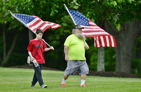 Jeff Lange | The Vindicator  MAY 25, 2015 - Army Vietnam veteran Thomas Moenich of Boardman and his grandson Samuel Arnold carry American flags as they make their way to Maag Outdoor Arts Theatre in Boardman Park, Monday morning during the Memorial Day celebration in Boardman.
