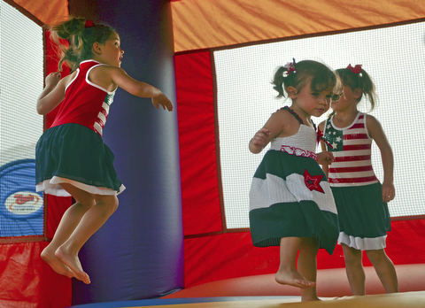 Katie Rickman | The Vindicator.Eva Lemke 1, center, jumps in the bounce house with her twin sisters Emma and Ella 5 at the Austintown Fireworks Celebration July 3, 2015.