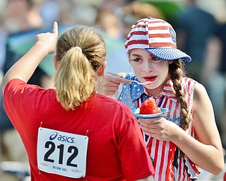 Jeff Lange | The Vindicator  JULY 4, 2015 - Dressed in her patriotic outfit, Aurora Fares of Canfield (right), gobbles down a snow cone as she chats with other festival goers prior to the start of Saturday morning's Fourth of July parade at the square in Canfield.
