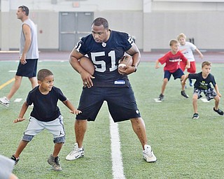 Jeff Lange | The Vindicator  JULY 11, 2015 - Former NFL linebacker and YSU Penguin Tim Johnson (center) coaches children during warmups at his annual football skills camp in Youngstown, Saturday morning. Pictured at Johnson's right in 6 year old Michael Wade of Niles.