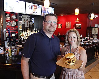 The owners of COACHES Burger Bar, Patrick Howlett and  Stacy Sam, posed with the burger of the month: the Big Texan