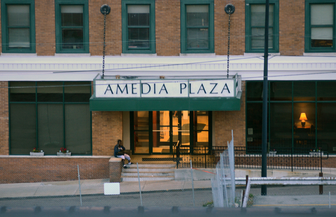 A person sits on the front stoop of the Amedia Plaza apartments on Hazel Street.