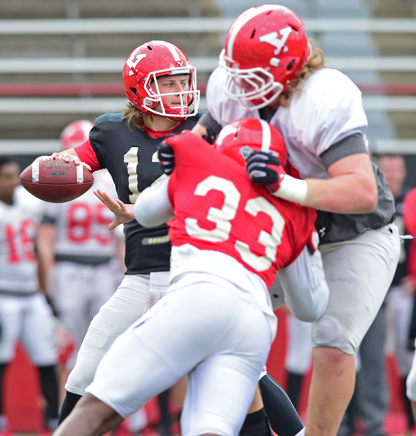 YOUNGSTOWN, OHIO - MARCH 23, 2016: Ricky Davis #12 of YSU throws a pass from the pocket behind the block of Jeff Rotheram (white) on Johnson Louigene (red) during the teams practice Wednesday afternoon at Stambaugh Stadium. DAVID DERMER | THE VINDICATOR