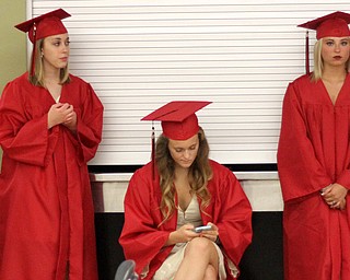 Nikos Frazier | The Vindicator..Maggie Beistel(center) looks at her phone before receiving her diploma from Canfield High School on Sunday, June 5, 2016.