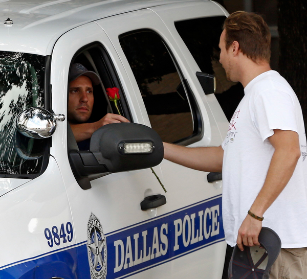 John Fife  hands a police officer guarding Jack Evans Police Headquarters a rose in Dallas on Friday July 8, 2016. Snipers opened fire on police officers in the heart of Dallas during protests over two recent fatal police shootings of black men. (Nathan Hunsinger | The Dallas Morning News via AP)
