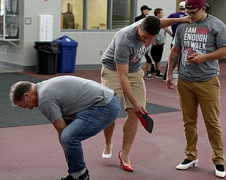 Joe Maxin, Assistant Mahoning County Prosecutor, bends over to put on his heels as Jordan Burke(center) leans on Adam Weis(right) to put on his heels before a Walk a Mile in Her Shoes at the Watts and Tressel Training Site at Youngstown State University, Friday, April 21, 2017 in Youngstown. ..(Nikos Frazier | The Vindicator)..