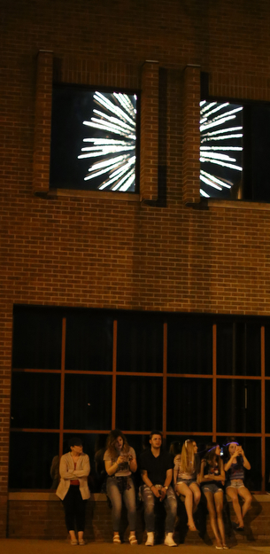 A group watches the fireworks display as the explosion is reflected in the window of a Front St. business during the Fourth of July Fireworks at the Covelli Centre, Tuesday, July 4, 2017 in Youngstown...(Nikos Frazier | The Vindicator)