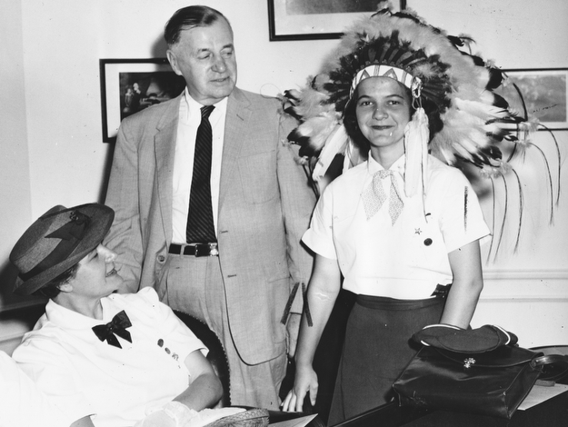 An Indian chief's headdress, one of many gifts to the Youngstown congressman, is tried on by Miss Sherry Evans of 1357 Thalia Ave. as the Girl Scouts visited Kirwan's office.