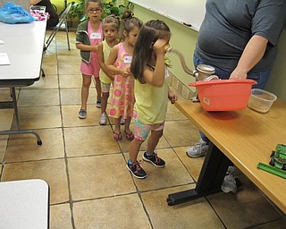 Neighbors | Alexis Bartolomucci.Children lined up to use the grinder on wheat seeds to turn them into flour after reading "The Little Red Hen" at Sprout Club.
