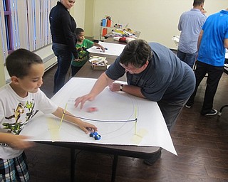 Neighbors | Zack Shively.Librarian Karen Saunders and a child raced their foam cars at Boardman library.  The foam cars did not roll very well, so they had to push or flick them. The children made their finish lines using tape, straws and strings.
