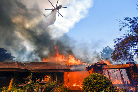 A helicopter dumps water on a home as firefighters battle a wildfire in Anaheim Hills in Anaheim, Calif., Monday, Oct. 9, 2017. Wildfires whipped by powerful winds swept through Northern California sending residents on a headlong flight to safety through smoke and flames as homes burned. (Jeff Gritchen/The Orange County Register via AP)