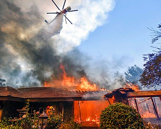 A helicopter dumps water on a home as firefighters battle a wildfire in Anaheim Hills in Anaheim, Calif., Monday, Oct. 9, 2017. Wildfires whipped by powerful winds swept through Northern California sending residents on a headlong flight to safety through smoke and flames as homes burned. (Jeff Gritchen/The Orange County Register via AP)