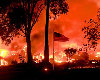 An American flag still fly's as as structures burn in Coffey Park, Monday Oct. 9, 2017. More than a dozen wildfires whipped by powerful winds been burning though California wine country. The flames have destroyed at least 1,500 homes and businesses and sent thousands of people fleeing. (Kent Porter/The Press Democrat via AP)