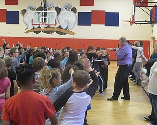 Neighbors | Zack Shively.The school had to do multiple assemblies throughout the week because of the size of their school. They did about three celebration ceremonies each day. Pictured, the students pretend to add ingredients to a stew based on principal Lenton's demonstration.