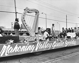 The luck of the Irish didn't keep the chilly temperatures away, so the riders on the Mahoning Valley Gaelic Society float use a blanket to keep warm while an Irish step dancer braves the biting winds to perform...Photo taken March 11, 1984...Photo by Robert K. Yosay - The Vindicator.