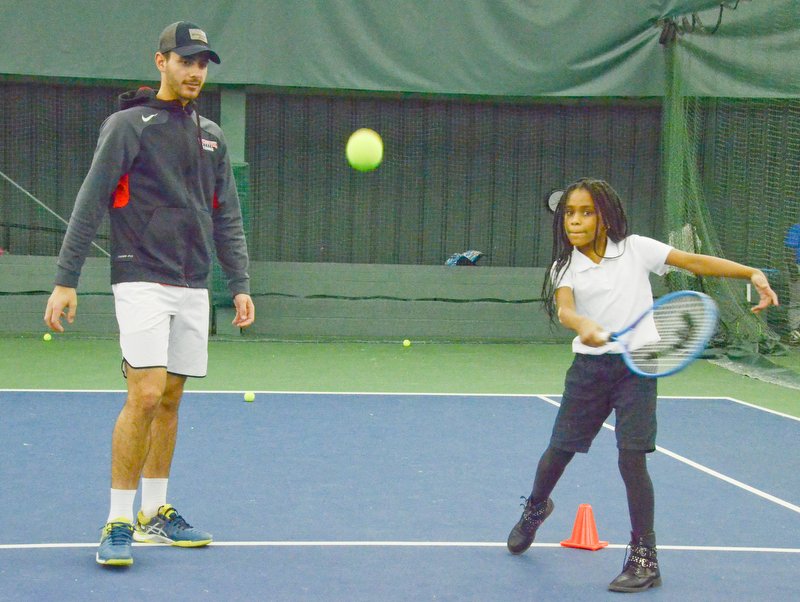Mercedes Haskins, age 10; from Youngstown Community School, whacks a tennis ball as Vasileios Vardakis, YSU freshman business major from Greece, observes at the Boardman Tennis Center on March 23, 2018.  

Photo by Scott Williams - The Vindicator.