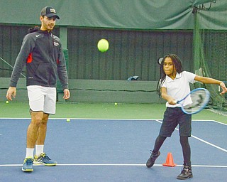Mercedes Haskins, age 10; from Youngstown Community School, whacks a tennis ball as Vasileios Vardakis, YSU freshman business major from Greece, observes at the Boardman Tennis Center on March 23, 2018.  

Photo by Scott Williams - The Vindicator.